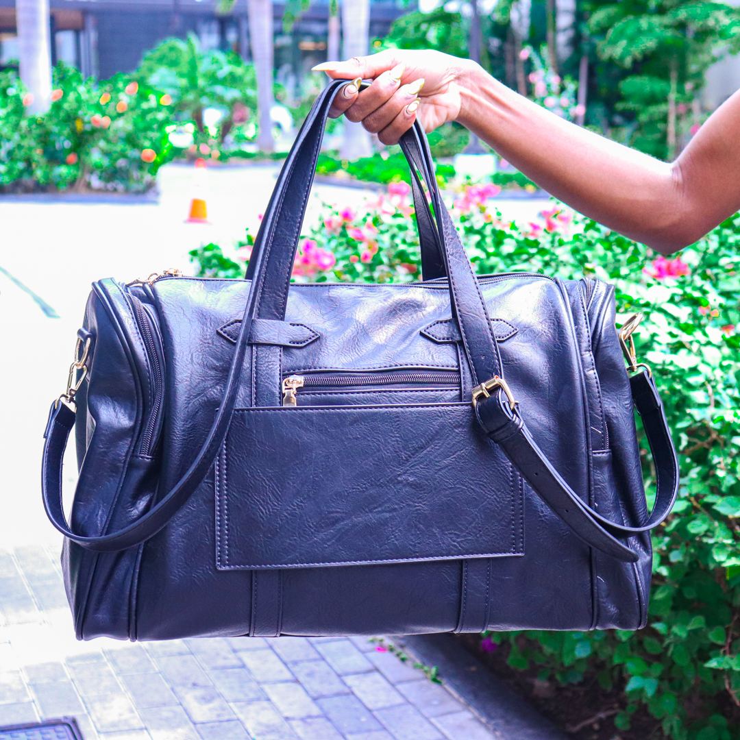 A Bag Depot customer holding a black vegan-leather travel duffle bag outdoors in New Kingston, Jamaica.
